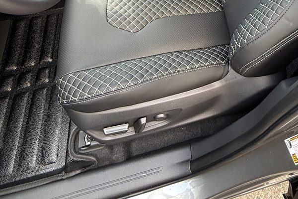 Ribbed black floor mat in a footwell beside a stitched seat cover